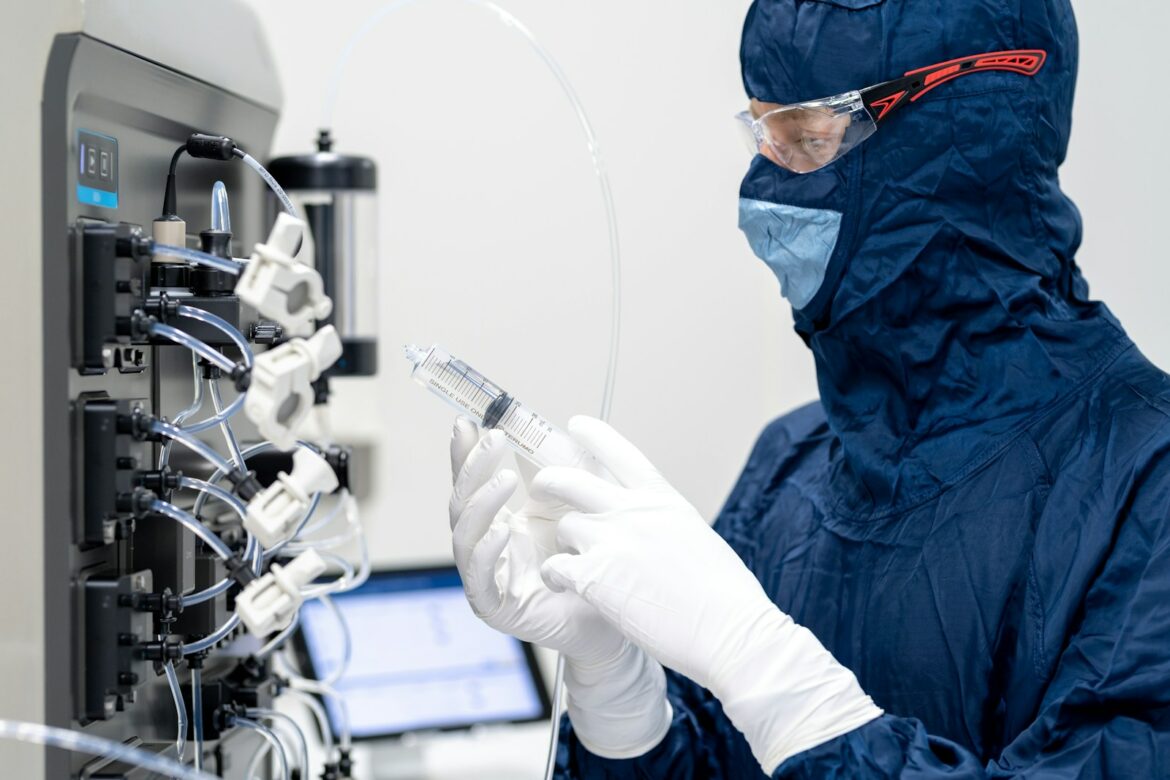 a person in a blue lab coat and gloves using a syringe